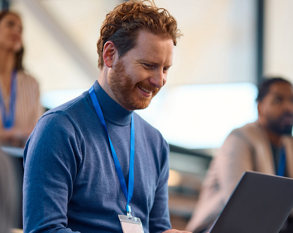 ACTICO Header Happy entrepreneur working on laptop while participation in business education event in conference hall.